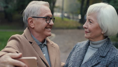 Vorderansicht-Eines-älteren-Ehepaares,-Das-Posiert-Und-In-Die-Kamera-Lächelt,-Während-Es-Bei-Sonnenuntergang-Ein-Selfie-Foto-Mit-Dem-Smartphone-Im-Park-Macht