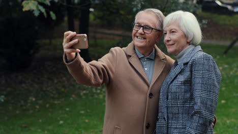 Älteres-Ehepaar-Posiert-Und-Lächelt-In-Die-Kamera,-Während-Es-Bei-Sonnenuntergang-Ein-Selfie-Foto-Mit-Smartphone-Im-Park-Macht-1