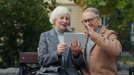älteres-Ehepaar-Sitzt-Auf-Der-Bank-Im-Park-Und-Hat-Im-Herbst-Einen-Videochat-Mit-Tablet