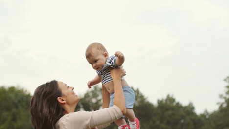 Happy-Mother-Tossing-Up-Her-Cute-Toddler-Son-In-The-Park