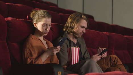 Couple-Sitting-In-Movie-Theater-And-Using-Mobile-Phone-Before-The-Film-Starts