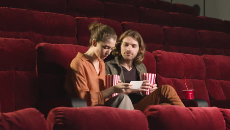 Couple-Sitting-On-The-Seats-In-The-Cinema-While-They-Holding-Popcorn-And-Drinks-And-Waiting-To-Watch-The-Movie