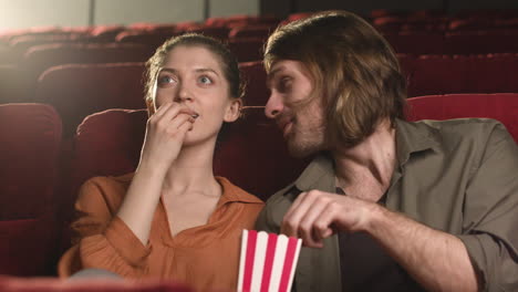 Glückliches-Paar-Sitzt-Im-Kino,-Während-Sie-Reden-Und-Popcorn-Essen-Und-Darauf-Warten,-Den-Film-Zu-Sehen