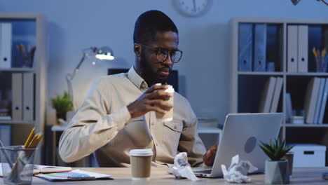 Young-Man-Working-With-Laptop-And-Drinking-Coffee-In-The-Office-At-Night