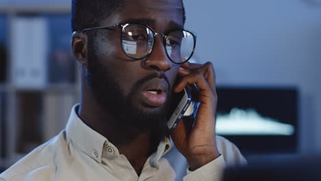 Close-Up-View-Of-Young-Man-In-Glasses-Talking-On-The-Phone-With-Sad-Or-Worried-Face-In-The-Office-At-Night