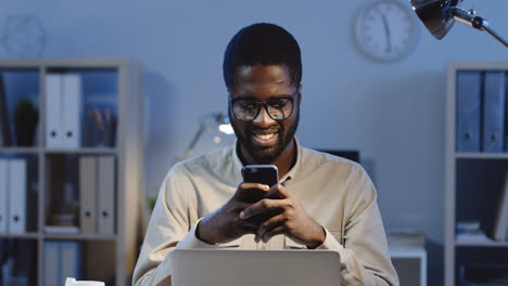 Close-Up-View-Of-Young-Man-In-Glasses-Chatting-On-The-Smartphone-And-Smiling-In-The-Office-At-Night