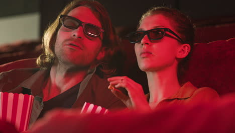 Nahaufnahme-Eines-Paares-Mit-3D-Brille,-Das-Im-Kino-Sitzt,-Während-Sie-Einen-Film-Ansehen-Und-Bei-Ausgeschaltetem-Licht-Popcorn-Essen