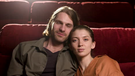 Couple-Sitting-In-The-Cinema-Smiling-And-Looking-At-Camera