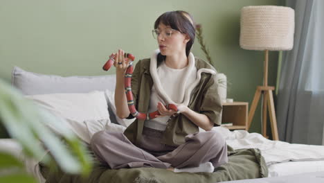 Happy-Young-Woman-Holding-Her-Two-Pet-Snakes-While-Sitting-On-Bed-At-Home