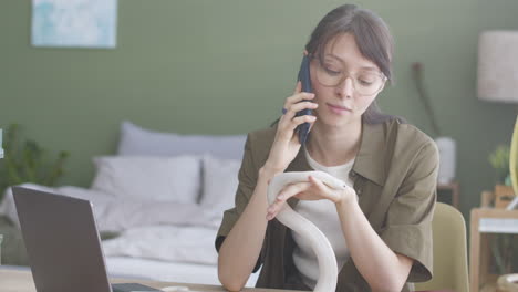 Young-Woman-Making-A-Phone-Call-And-Holding-Her-White-Pet-Snake-While-Sitting-At-Table-At-Home