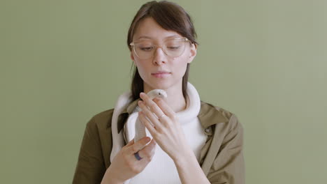 Portrait-Of-A-Young-Woman-With-Eyeglasses-Holding-A-White-Pet-Snake-Around-Her-Neck-And-Hands-On-A-Green-Background