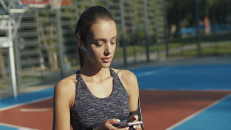 Sporty-Girl-With-Airpods-Laughing-While-Texting-Message-On-Smartphone-At-Outdoor-Court-On-A-Summer-Day-1