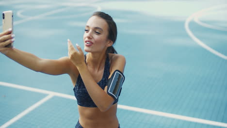 Fitness-Frau-Bläst-Luftkuss-Und-Nimmt-An-Einem-Sommertag-Auf-Dem-Sportplatz-Ein-Selfie-Auf-Dem-Smartphone
