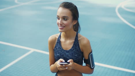 Sporty-Girl-With-Airpods-Laughing-While-Texting-Message-On-Smartphone-At-Outdoor-Court-On-A-Summer-Day-2