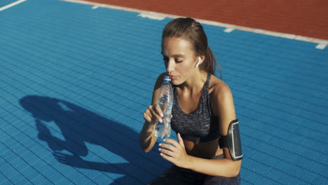 Fitness-Woman-Sitting-At-Sport-Court-And-Drinking-Cold-Water-After-Workout-On-A-Summer-Day-1
