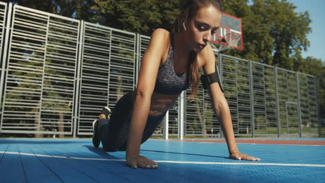 Focused-Fitness-Girl-With-Airpods-Doing-Push-Ups-At-Sport-Court-On-Summer-Day