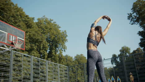 Rear-View-Of-A-Sporty-Woman-Warming-Up-And-Stretching-Back-At-Outdoor-Basketball-Court