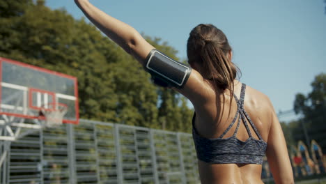 Rear-View-Of-A-Sporty-Woman-Warming-Up-Her-Arm-At-Outdoor-Basketball-Court-On-A-Sunny-Morning