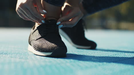 Close-Up-Of-Female-Feet-In-Black-Trainers-Jogging-On-Sport-Court-On-Sunny-Day-And-Then-Hands-Fixing-Laces