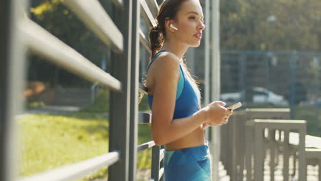 Side-View-Of-A-A-Pretty-Sportswoman-Texting-Message-On-Smartphone-And-Laughing-At-Outdoor-Court-On-A-Summer-Day