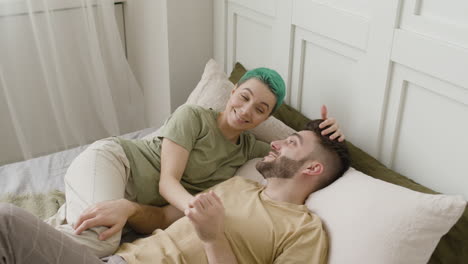Smiling-Woman-Caressing-Her-Boyfriend's-Hair-And-Talking-With-Him-While-Lying-Together-On-The-Bed