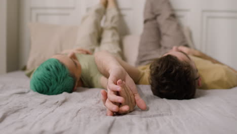 Loving-Couple-Holding-Hands-And-Looking-At-Each-Other-While-Lying-On-A-Cozy-Bed-With-Their-Legs-Up-On-The-Wall-1