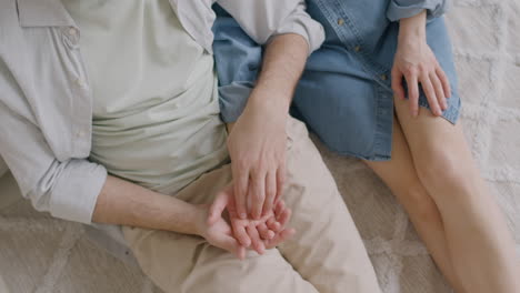 Unrecognizable-Man-Tenderly-Touching-His-Girlfriend's-Hand-While-Sitting-Together-On-A-Carpet-At-Home