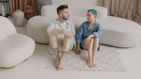 Barefoot-Couple-Holding-Hands-And-Talking-Together-While-Sitting-On-A-Carpet-At-Home