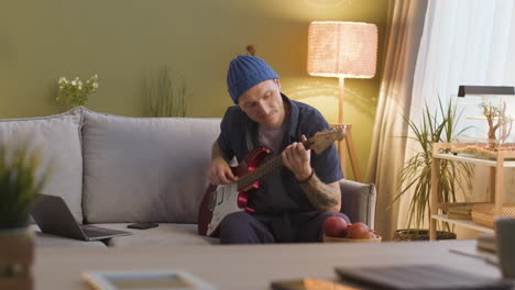 Distant-View-Of-Man-Sitting-On-A-Sofa-While-Playing-The-Electric-Guitar