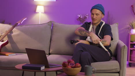 Man-Sitting-On-Sofa-And-Holding-A-Snake-Around-His-Neck-While-Playing-Video-Games-On-The-Laptop
