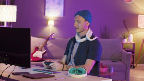 Man-Sitting-At-Desk-And-Holding-A-Snake-Around-His-Neck-While-Playing-Video-Games-On-The-Computer
