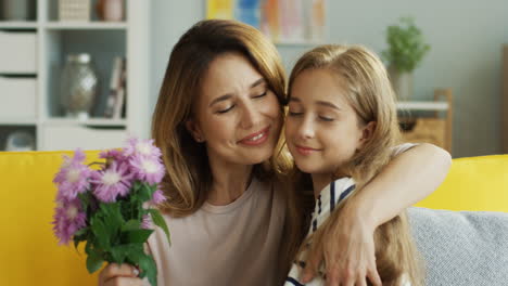 Close-Up-Of-Teenager-Girl-Giving-Flowers-To-Her-Mother-And-Hugging-Her-On-The-Sofa-In-The-Living-Room