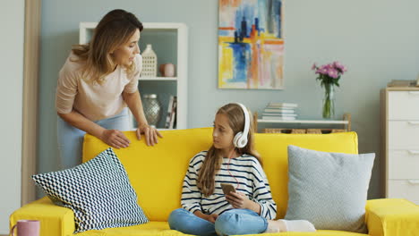 Teenage-Girl-With-Headphones-Listening-To-Music-Sitting-On-Yellow-Sofa-While-Her-Mother-Speaks-Loud-To-Her-1