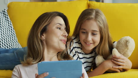 Close-Up-View-Of-Blonde-Mother-With-Her-Teen-Daughter-Watching-Something-On-A-Tablet-And-Smiling