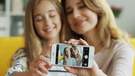 Close-Up-View-Of-Mother-And-Cute-Girl-Taking-A-Selfie-With-Smartphone-Sitting-On-Sofa-In-Living-Room