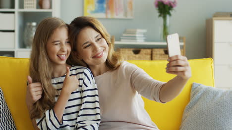 Nahaufnahme-Der-Mutter-Und-Des-Süßen-Mädchens,-Die-Ein-Selfie-Mit-Dem-Smartphone-Machen,-Das-Auf-Dem-Sofa-Im-Wohnzimmer-2-Sitzt