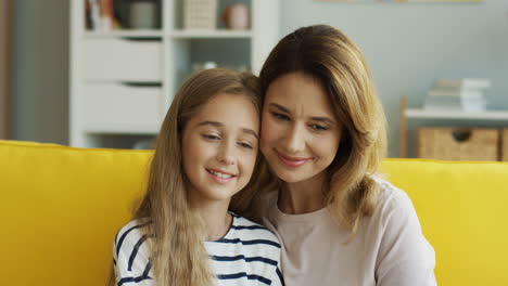 Close-Up-View-Of-Woman-Hugging-Her-Cute-Teen-Daughter-While-They-Sitting-On-Couch-And-Watching-Something-In-Living-Room