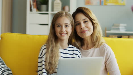 Blonde-Mother-And-Daughter-Sitting-On-Sofa-While-Watching-Something-On-Computer