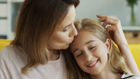 Close-Up-View-Of-Woman-Hugging-Her-Cute-Teen-Daughter-While-They-Sitting-On-Couch-And-Watching-Something-On-Laptop-In-Living-Room