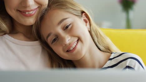 Close-Up-Of-The-Cute-Teenage-Girl-Leaning-On-Her-Mother's-Shoulder-While-Watching-Something-On-Laptop-In-Living-Room