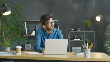 Junger-Arabischer-Mann,-Der-Am-Schreibtisch-Mit-Kaffee-Zum-Mitnehmen-Und-Schreibwaren-Vor-Dem-Laptop-Im-Büro-Sitzt