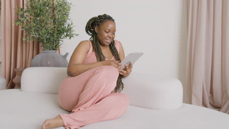 Woman-With-Braids-Sitting-On-A-Big-Sofa-While-Using-A-Tablet
