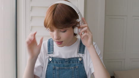Close-Up-View-Of-Girl-Sitting-On-Windowsill,-Then-She-Puts-The-Headphones-And-Plays-Music-From-Her-Smartphone