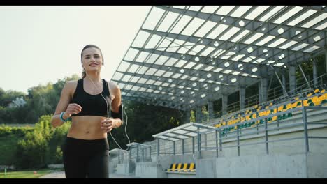 Young-Jogger-Woman-Listening-To-The-Music-With-Headphones-While-Jogging-In-The-Stadium-On-A-Summer-Day