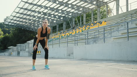 Young-Jogger-Woman-Running-In-The-Morning-In-The-Stadium,-Then-Stops,-Breaths-And-Rests-For-A-Minute
