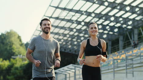 Close-Up-View-Of-Young-Jogger-Couple-Running-Together-Listening-To-Music-With-Headphones-In-The-Stadium-On-A-Summer-Morning-1