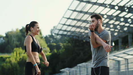 Young-Jogger-Couple-Exercising-And-Warming-Up-Hands-And-Shoulders-In-The-Stadium-In-Summer