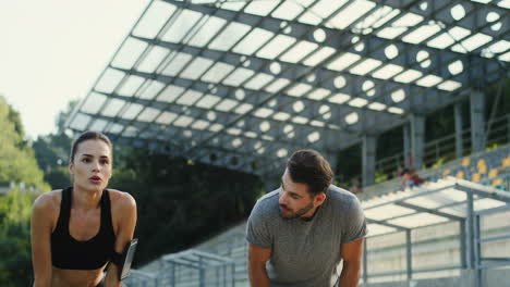 Young-Jogger-Couple-Running-In-The-Stadium,-Then-They-Stop-To-Have-A-Rest-And-Look-At-Camera