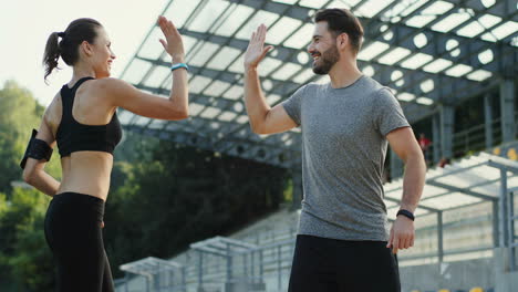Young-Jogger-Couple-Running-In-The-Stadium,-Then-They-Stop-And-Look-At-Camera