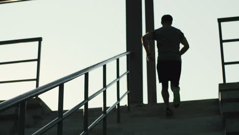 Rear-View-Of-Young-Jogger-Man-Running-Up-The-Stairs-In-The-Stadium-On-A-Summer-Day